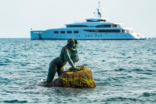Sculpture of a mermaid with a child in her arms, in the sea on a stone on the background of a ship. Mishor, Crimea.