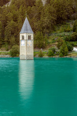 The old bell tower of Curon (Graun) emerging from the emerald waters of Lake Resia, South Tyrol, Italy