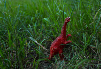 a toy dinosaur stands among the green grass