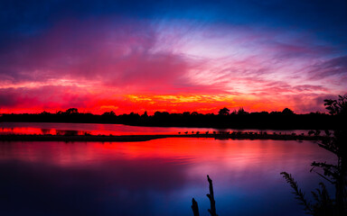Nightscape photo of wildlife sanctuary lagoon after blazing red sunset with dramatic clouds floating. Tranquil landscape with migrating birds nesting on the sandbar isle in the middle of the lake.