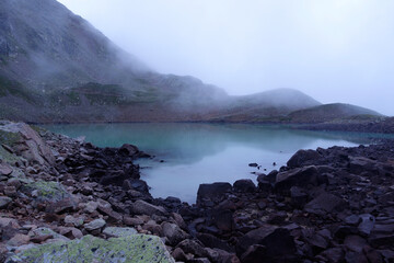 Alpine lake in the clouds. Alpine lake with rocky shores and emerald water in the clouds. Alpine lake Giybashkel (3240 meters above sea level), Caucasus. 