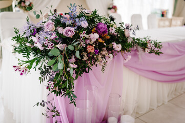 The composition of purple, pink flowers and greenery standing on served table in the area of wedding party. Close up.