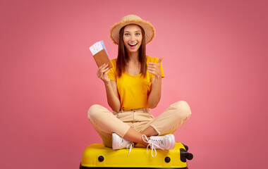 Excited girl sitting on suitcase, holding passport with tickets