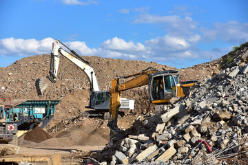Excavator load concrete waste into a mobile jaw crusher machine at at landfill. Disposal of...