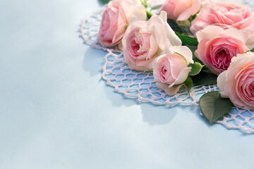 Flowers pink roses on openwork napkin on a blue paper background with space for text