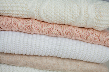 Fototapeta na wymiar A stack of knitted sweaters, cotton. Women's sweaters lie on the ottoman. Cozy autumn clothes.