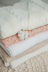 Fototapeta na wymiar A stack of knitted sweaters, cotton. Women's sweaters lie on the ottoman. Cozy autumn clothes.