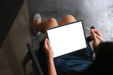 Cropped shot woman sitting and looking at digital tablet device with white blank screen at home.