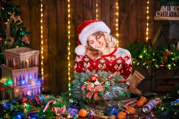 Woman making handmade christmas wreath on table. Christmas decoration and composition. Girl dressed in christmas design sweater prepare christmas wreath for holiday.