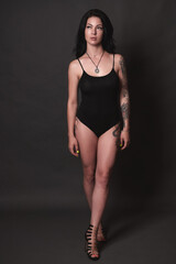 Fototapeta na wymiar Tattooed brunette in black swimsuit on black background