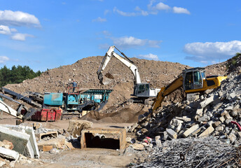 Fototapeta premium Excavator load concrete waste into a mobile jaw crusher machine at at landfill. Disposal of construction waste. Recycling concrete and asphalt from demolition.