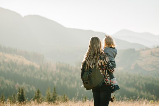 Mother and child with a backpack enjoying the sunset in the mountains.The concept of family travel, adventure, and tourism.  Lifestyle and hiking autumn vacations outdoor. Back view.