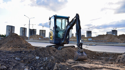 Obraz premium Mini excavator digg trench to lay cables concrete curbs and paving slabs at construction site. Backhoe on earthwork/roadworks