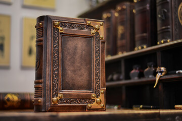 Leather book over wooden table, books in the background and pictures on the wall