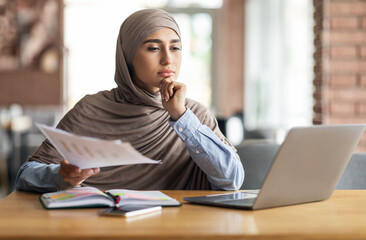 Pensive muslim woman manager working while sitting at cafe