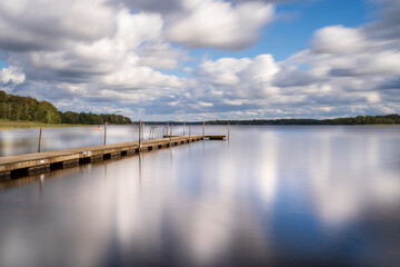 Fototapeta na wymiar Long exposure over jetty and lake with clouds and reflection. Location is Vastersjon, Sweden.