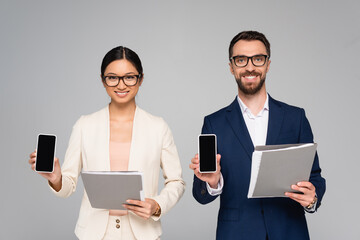 couple of interracial business colleagues holding folders and smartphones with blank screen isolated on grey