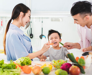 parent feeding boy a piece of  carrot in kitchen