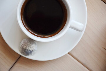 White porcelain cup of coffee on a saucer and candy in foil