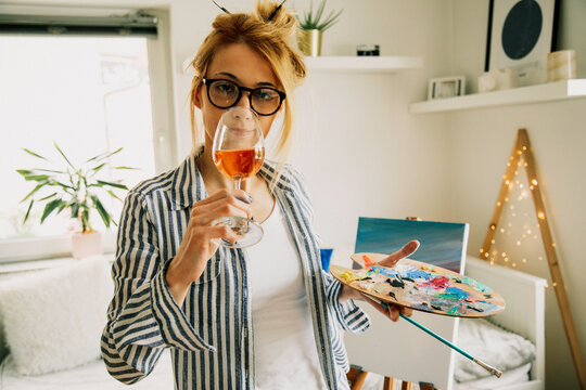 Beautiful artist woman painting in her room while drinking wine.