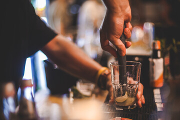Fototapeta na wymiar Dettaglio mani di barista che prepara un cocktail su di un bancone di un locale serale