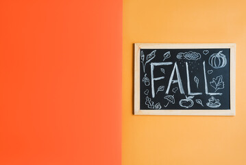 Blackboard with handwritten text "Fall" and small simple autumn themed chalk art on orange background, top view, space for text