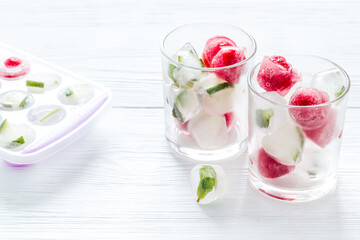 Cocktail glasses with berries in ice cubes on white table