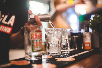 Dettaglio primo piano di mano di barista che prepara un cocktail versando dell'alcol nel bicchiere con ghiaccio in un locale notturno all'aperto