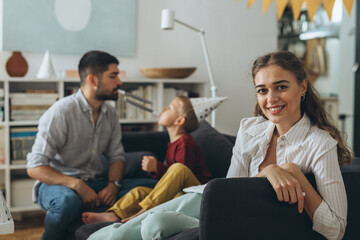 portrait of woman sitting sofa at home, father and boy are in blurred background