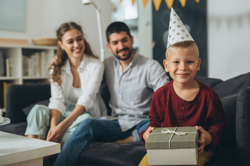 portrait of little boy holding present box, mother and father in blurred background