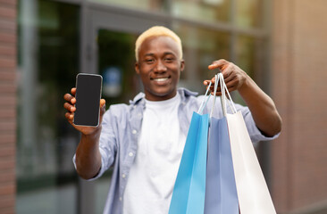 Happy african american man showing bags after shopping and smartphone with blank screen