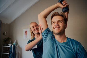 Obraz premium Portrait of handsome young smiling man exercising using dumbbells with female physiotherapist 