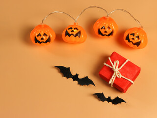 flat lay of red gift box with black paper bats and Halloween pumpkin lights on orange background with copy space. Halloween present concept.
