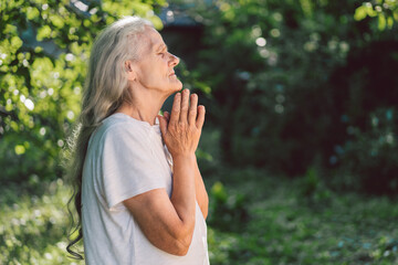 Fototapeta premium The gray-haired grandmother is praying in outdoors. Faith, spirituality and religion concept. 