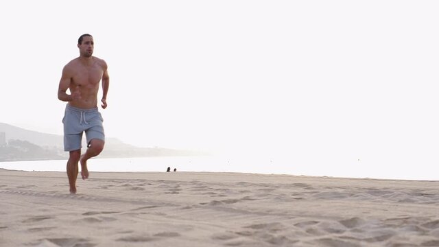 Fitness Male running at the beah at sunrise. Summer workout outdoors. Fit man doing exercise in the morning. Healthy lifestyle. Sports coach training alone