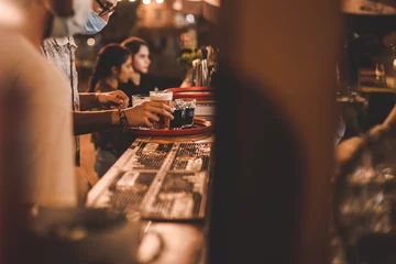 Photo sur Plexiglas Café Le barman avec masque le soir sert une bière sur un plateau au comptoir d& 39 un bar en bois extérieur