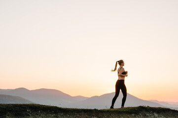 Athlete woman running on the road in the mountains. Runner fitness girl in sport tight clothes. Bright sunrise or sunset and blurry background. Horizontal. Workout wellness concept. Back view.