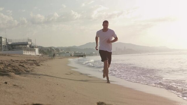 Fitness Male running at the beah at sunrise. Summer workout outdoors. Fit man doing exercise in the morning. Healthy lifestyle. Sports coach training alone