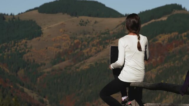 Girl is a freelancer working in nature in the mountains. She sits against the backdrop of the mountains with a laptop on her lap. The girl closes the laptop, finishing work. High quality 4k footage
