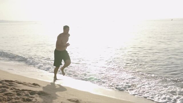 Fitness Male running at the beah at sunrise. Summer workout outdoors. Fit man doing exercise in the morning. Healthy lifestyle. Sports coach training alone