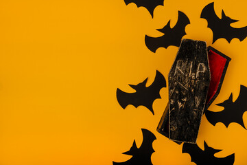 Halloween background in yellow color with silhouettes of bats and a small wooden black coffin. Flat lay with place for text.