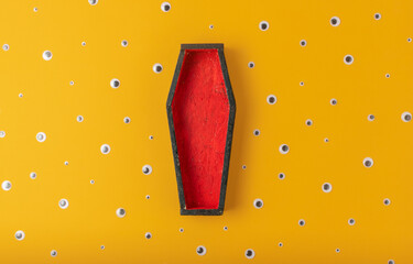 Halloween yellow background with an open red-black coffin in the center, around a scattering of plastic eyes of different sizes. A place for your product. - obrazy, fototapety, plakaty