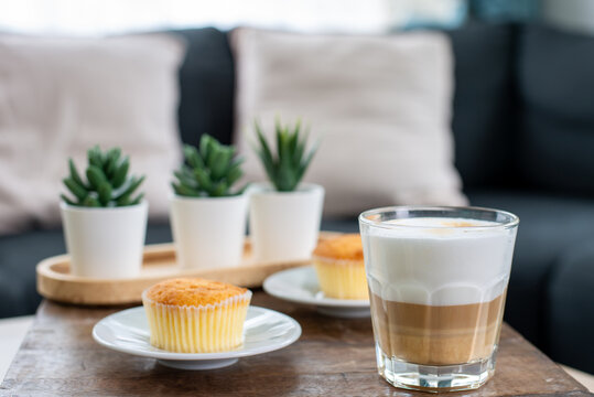 A good cup of cappuccino coffee with small cake served on a wooden table in the living room, afternoon coffee break