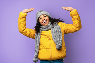 Cheerful Black Girl Holding Invisible Object Above Head, Purple Background