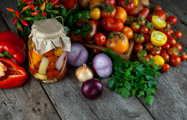 Tomatoes, peppers, onions on the table. Preservation of the autumn harvest of vegetables. Glass jar with pickled tomatoes. Wooden background. Vegetable food. Still life. Tomato of different varieties.