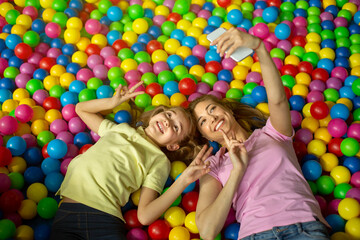 Fototapeta na wymiar Overhead view of adorable girl and her mom taking selfie on smartphone in ball pit at kids playground
