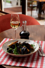 Mussels with spinach and balsamic vinegar with a glass of white wine, wooden table and italian red and white table cloth