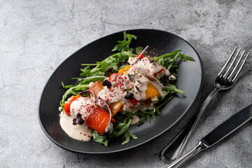 A black dish with baked vegetable rolls on grey stone background
