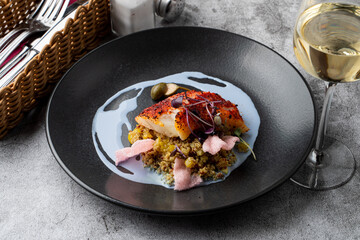 Gourmet special in a fancy restaurant: fried cod fillet with couscous and blue sauce on a wide black plate