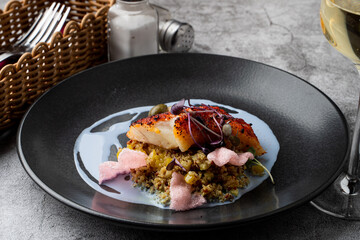Gourmet special in a fancy restaurant: fried cod fillet with couscous and blue sauce on a wide black plate